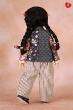 A doll viewed from the back wearing a dark navy patterned vest over a floral long-sleeve top, cream and gray vertically striped pants, and black shoes, against a soft peach studio background.
