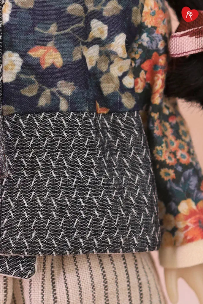 Close-up detail of a doll outfit featuring a navy floral jacket with a dark gray patterned cuff and a striped beige skirt.