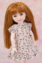 A doll with long auburn hair and a floral pink dress, posed against a soft pink textured background.