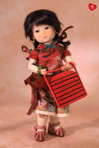 A collectible doll with dark hair, wearing a red floral dress and holding a red striped handbag, set against a warm beige studio background.